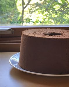 a chocolate cake sitting on top of a white plate next to a window sill