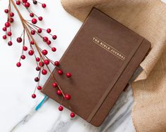 a brown notebook sitting on top of a white table next to red berries and a blue pen