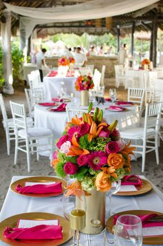 the table is set with white linens, pink and orange flowers in a vase