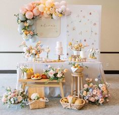 a table topped with lots of food next to a wall covered in balloons and flowers