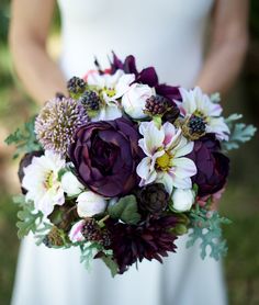 a bride holding a purple and white bouquet in her hand with other flowers on it