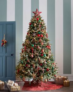 a decorated christmas tree with red, green and gold ornaments on it in front of a striped wall