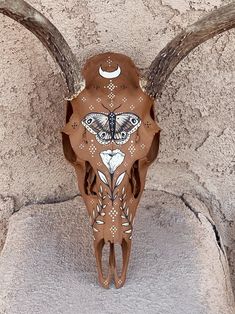 an animal skull with long horns and a butterfly painted on it's face sits in front of a stone wall