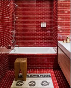 a bathroom with red tiles and a white bathtub next to a wooden stool on a rug