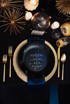 a black table topped with a plate and silverware next to candle holders filled with candles