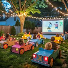 children are sitting in toy cars on the lawn at night with lights strung around them