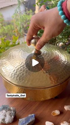 a person holding a large metal bowl on top of a wooden table next to rocks