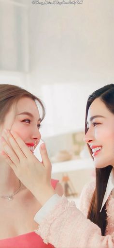 two young women are smiling and touching each other's faces in front of a mirror