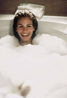 a woman smiles as she takes a bubble bath