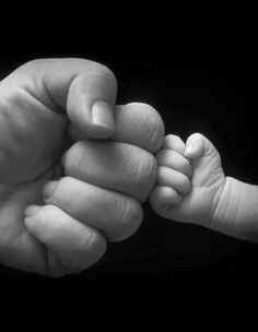 a black and white photo of a baby's hand holding the finger of an adult