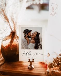 a couple kissing in front of a photo on a table next to a vase with dried flowers