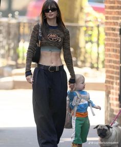 a woman walking down the street with a small child and a pug on a leash