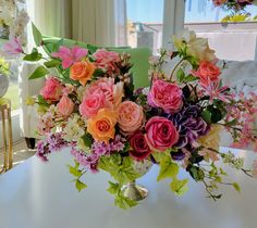 a vase filled with lots of colorful flowers on top of a table next to a window