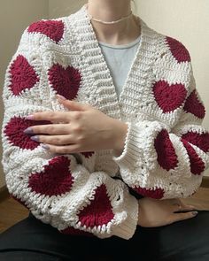 a woman wearing a white and red crocheted sweater with hearts on it, holding her hands together