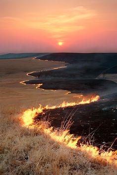 the sun is setting over an open field with grass and fire coming out of it