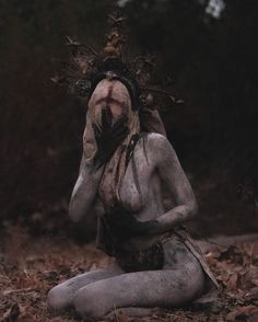 a woman with white paint on her face and body is sitting in the middle of leaves