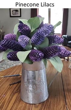 purple flowers are in a silver vase on a wooden table near a couch and window