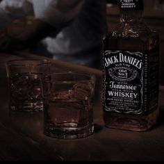 a bottle of jack daniels whiskey sitting on top of a table next to two glasses