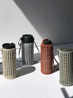 three crocheted cups are lined up on a white surface and one has a black lid