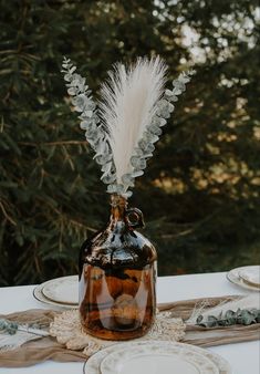 a vase with some feathers in it sitting on a table next to plates and napkins