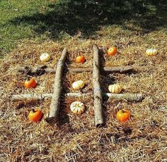 pumpkins and logs arranged in the shape of a cross on hay with grass around them