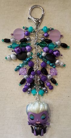 a key chain with a purple mask and beads hanging from it's side on a table