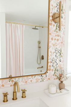 a bathroom sink with a large mirror above it and a pink flowered wallpaper