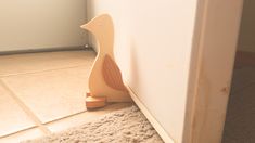 a wooden toy duck on the floor next to a white wall in a room with beige carpet