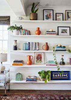 a living room filled with lots of books and vases on top of white shelves