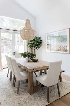 a dining room table with white chairs and a potted plant in the middle of it