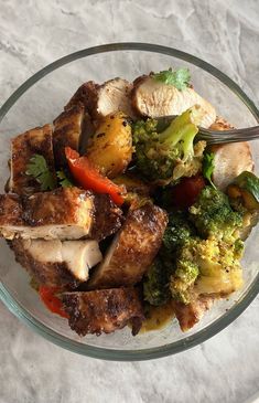 a glass bowl filled with meat and veggies on top of a white table