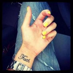 a woman's hand with a yellow and black tattoo on her wrist that says faith