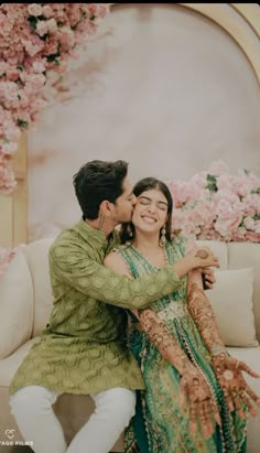 a man and woman sitting next to each other in front of a flower covered wall