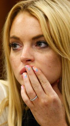 a blonde woman with blue and pink nail polish holding her hand up to her mouth