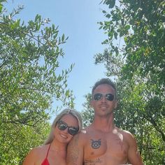 a man and woman standing next to each other in front of trees with tattoos on their arms