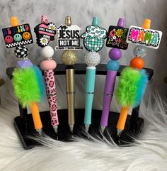 several different pens are lined up on a black holder with colorful pom - poms