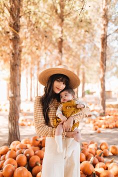 a woman holding a baby in her arms surrounded by lots of pumpkins and trees