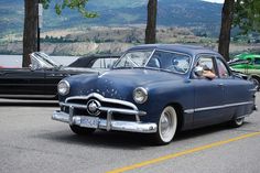 an old blue car driving down the road with other cars in the backround