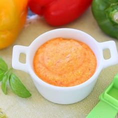 a small white bowl filled with sauce next to peppers and bell peppers on a table