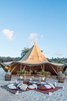 an outdoor tent set up on the beach with pillows and rugs around it for seating