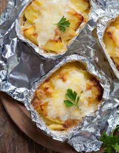 four baked potatoes with cheese and parsley in foil on a wooden plate next to parsley