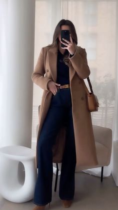 a woman taking a selfie in front of a window while wearing a coat and pants