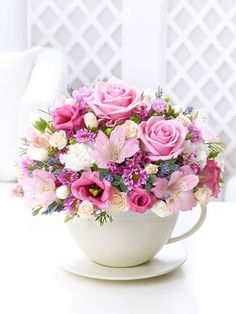 a white cup filled with pink flowers on top of a table