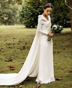 a woman in a white wedding dress holding a bouquet and standing next to a tree