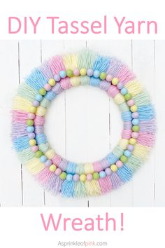 a multicolored wreath with tassels hanging on a white wooden wall in the shape of a circle