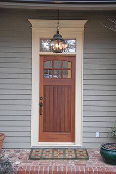 the front door of a house with potted plants on the steps and light fixture above it