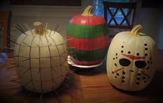 three painted pumpkins sitting on top of a wooden table