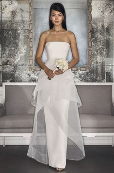 a woman in a white wedding dress standing next to a couch