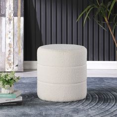 a white round ottoman sitting on top of a rug next to a potted plant