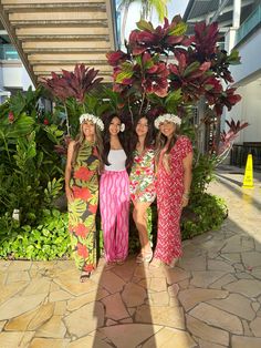 three women standing next to each other in front of plants and flowers on the ground